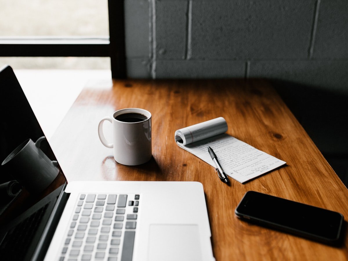 A quiet desk with coffee, an open notebook and morning light